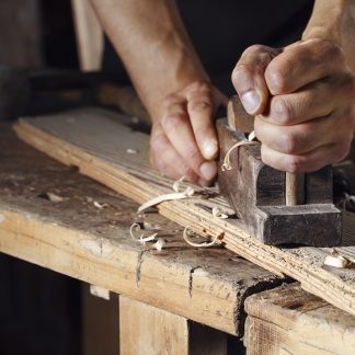 carpenter planing a plank of wood with a hand plane